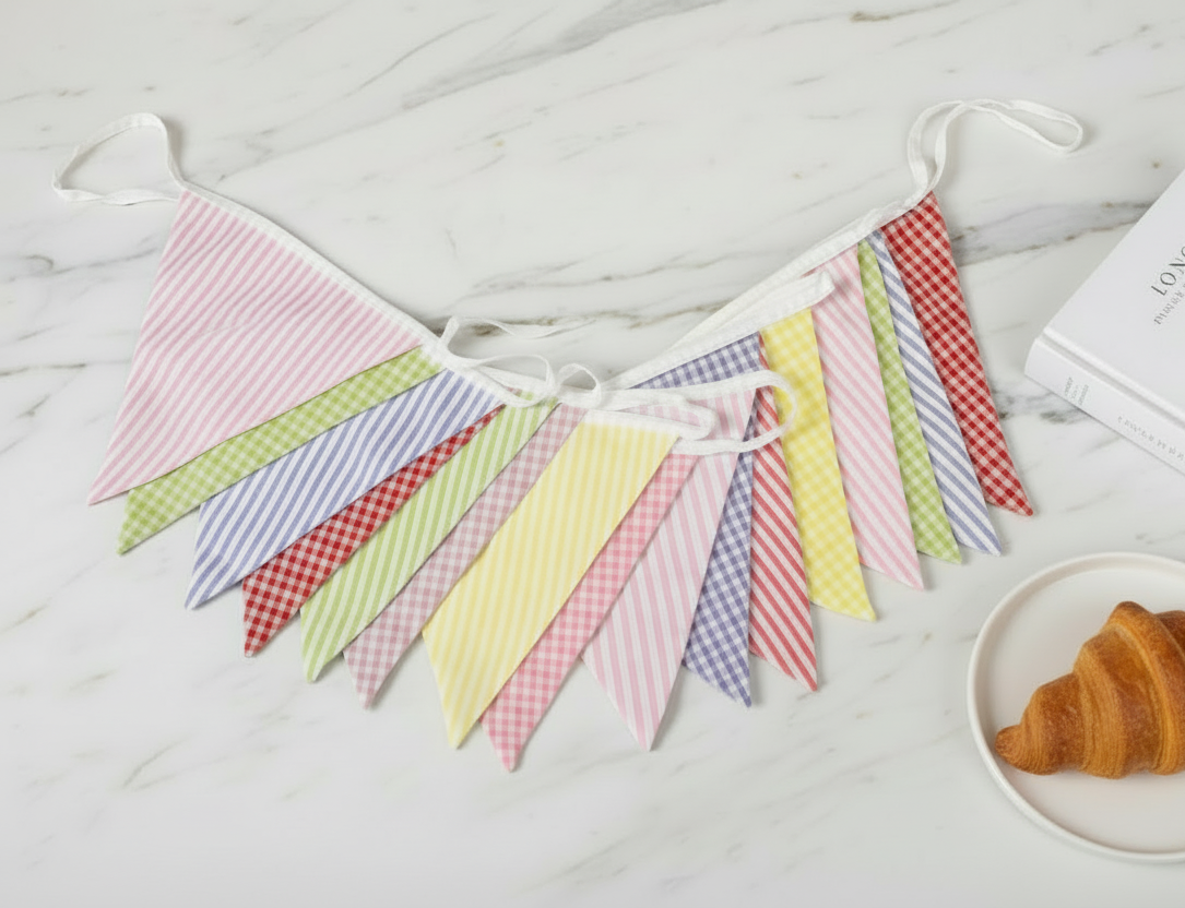 Pastel colored fabric bunting on a white wooden surface with a croissant in the background.