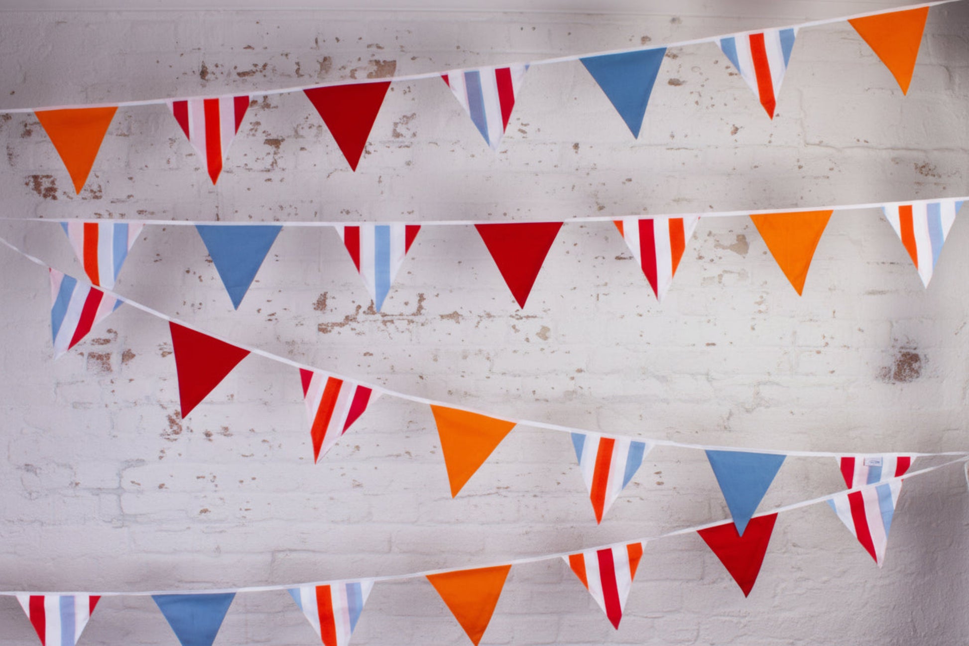 Colorful triangular flags hanging against a light gray brick wall.
