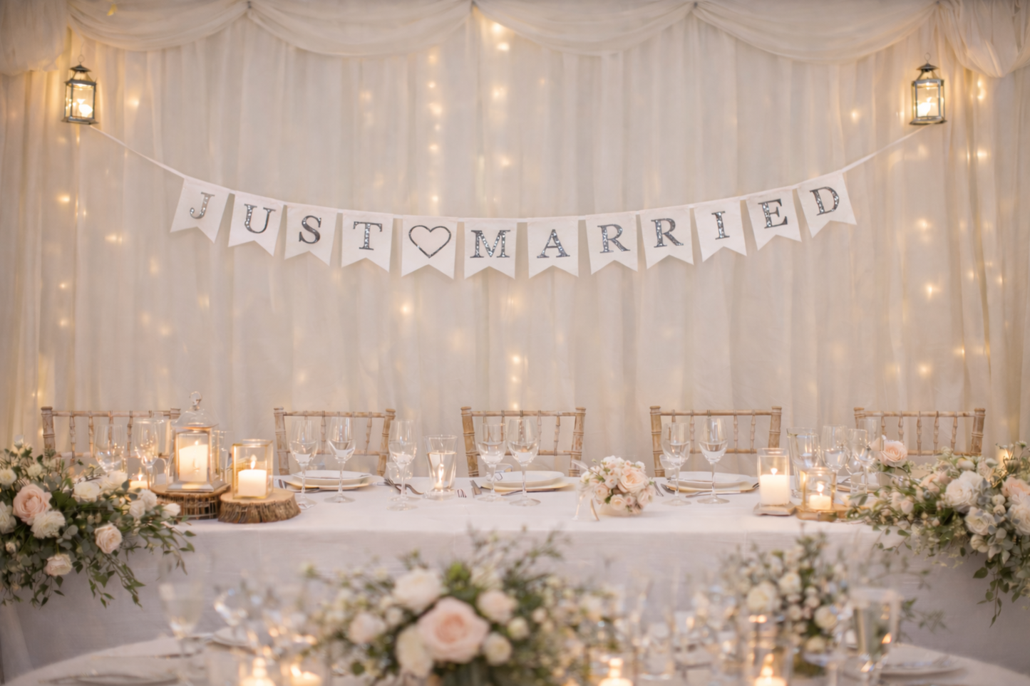 Decorated wedding table with 'Just Married' banner against a draped fabric wall with string lights.