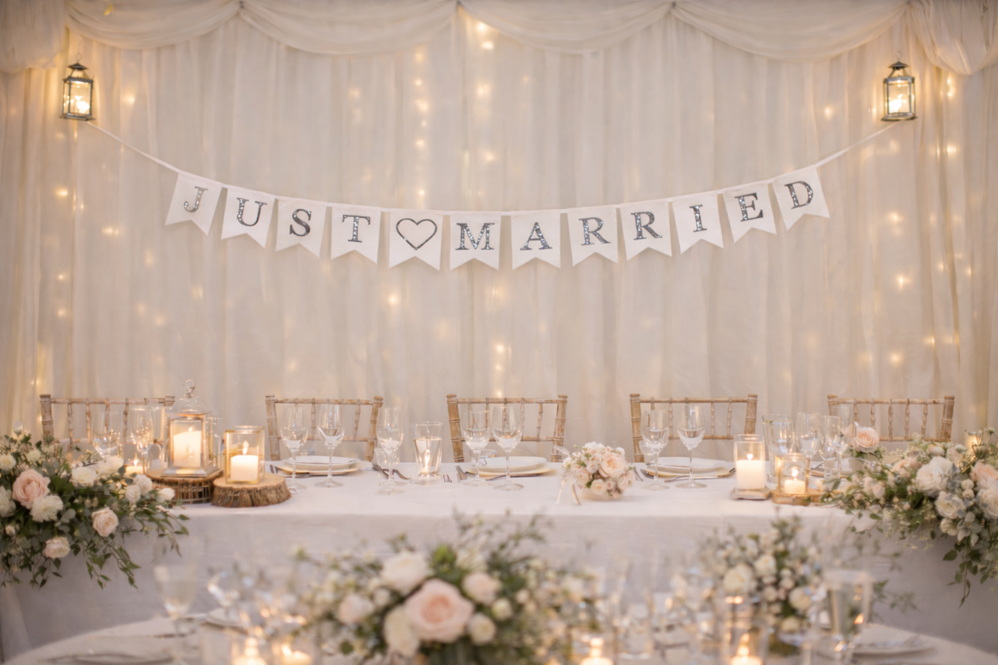 Decorated wedding table with 'Just Married' banner against a draped fabric wall with string lights.