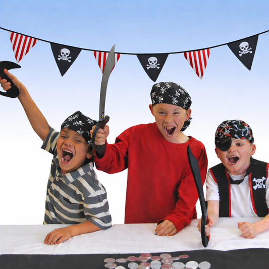 Three children in pirate costumes with pirate bunting flags and swords against a blue sky.